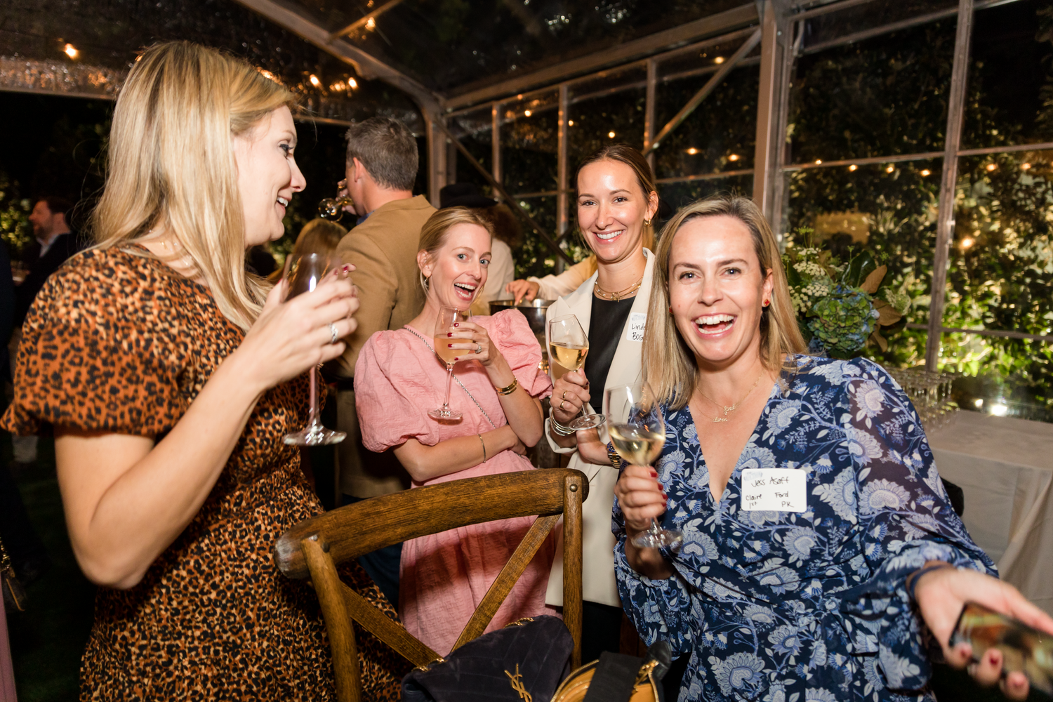 Group of friends laughing and socializing at an evening party with string lights overhead.
