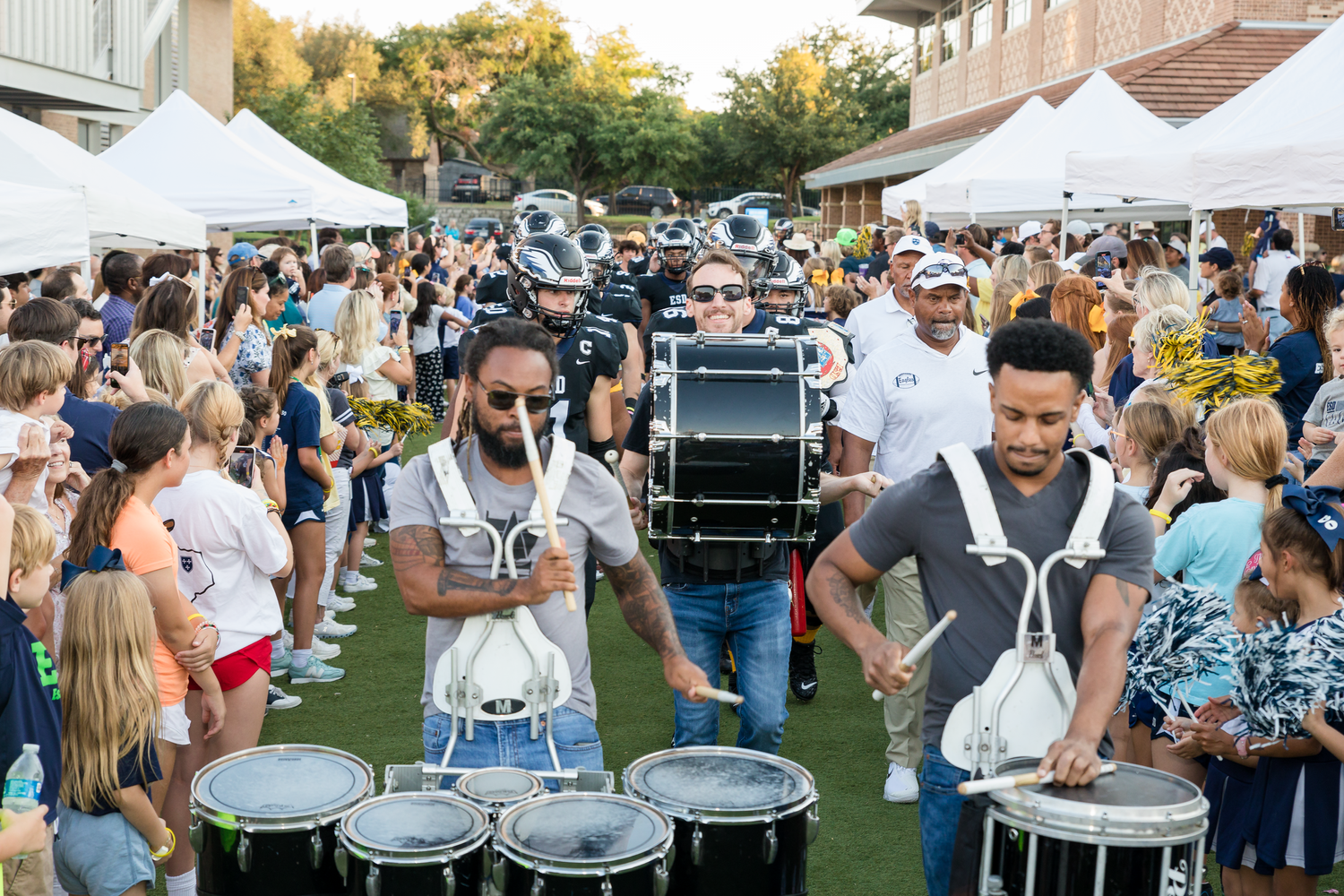 Outdoor event with white tents and crowd gathering near percussion instruments.