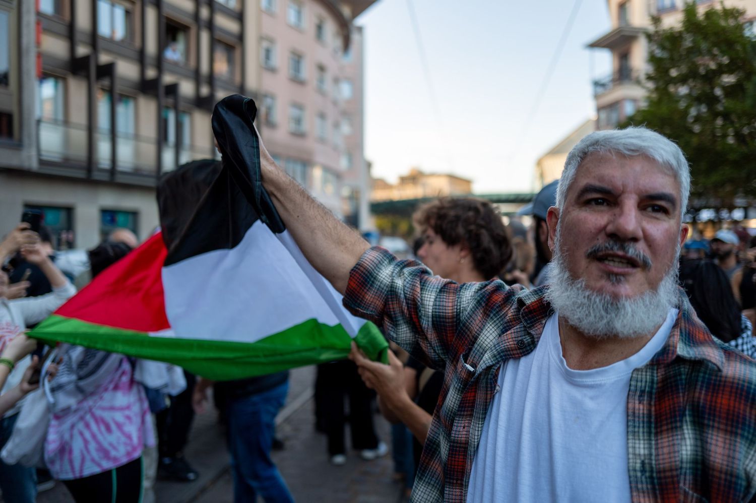 Person holding Palestinian flag at outdoor demonstration.