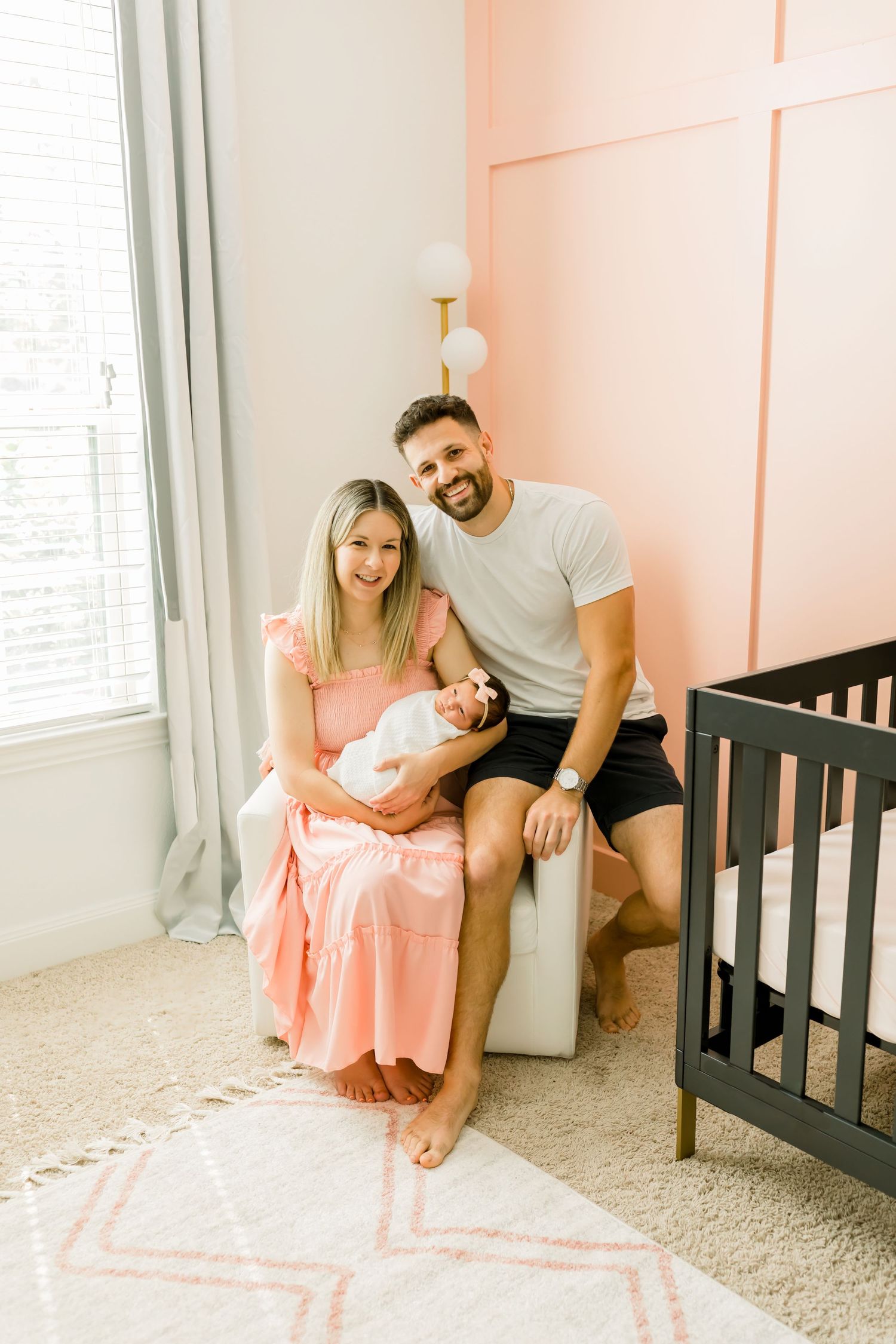 A family poses in a nursery with coral pink walls and a black crib.