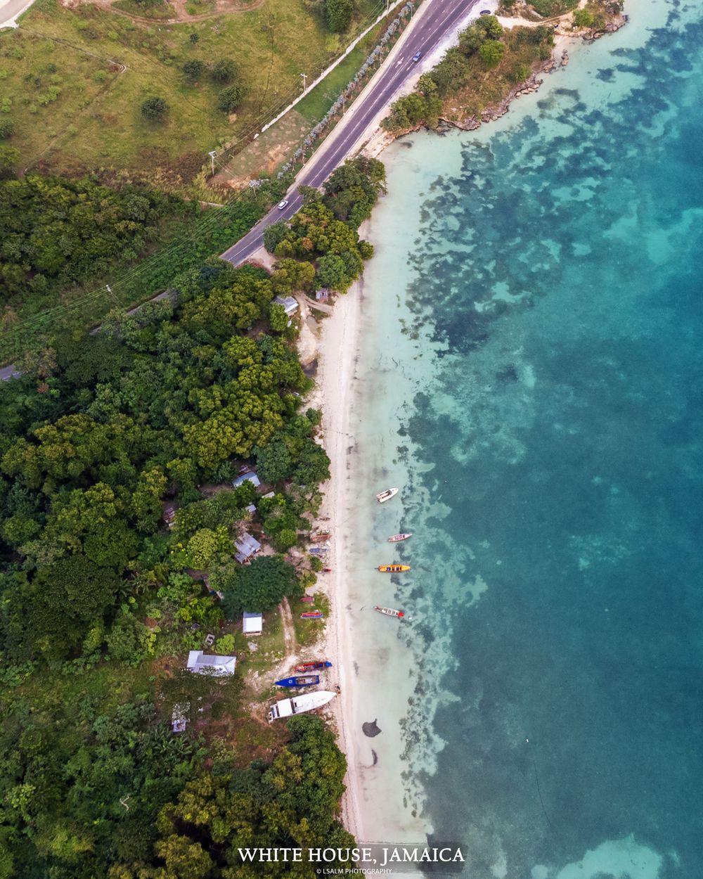 Aerial view of coastal road alongside turquoise waters and white sand beach.