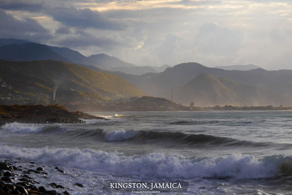 Dramatic sunset over Kingston coastline with waves crashing against rocky shore.