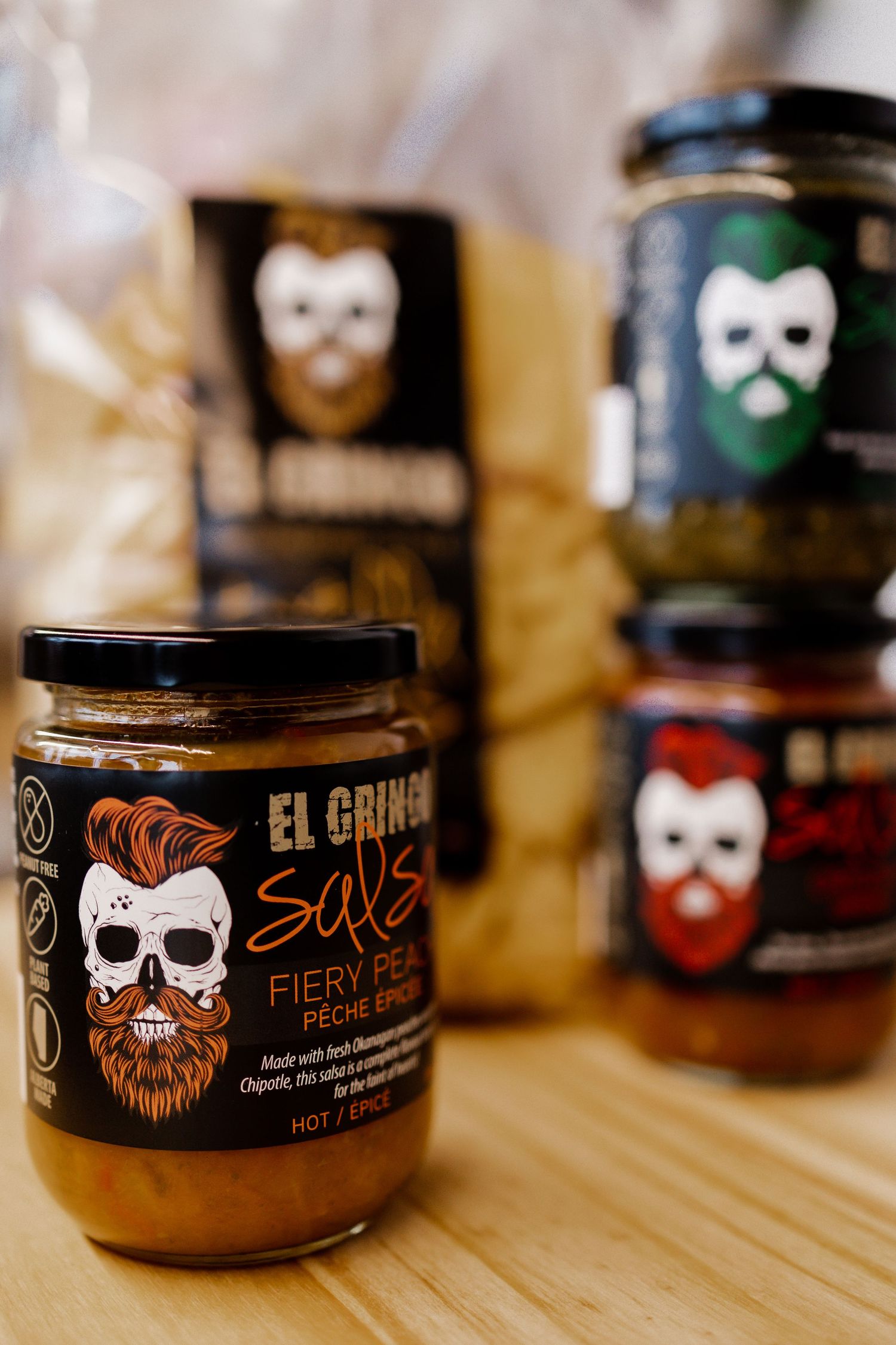 Hot sauce jars with skull logos and branding displayed on wooden surface.