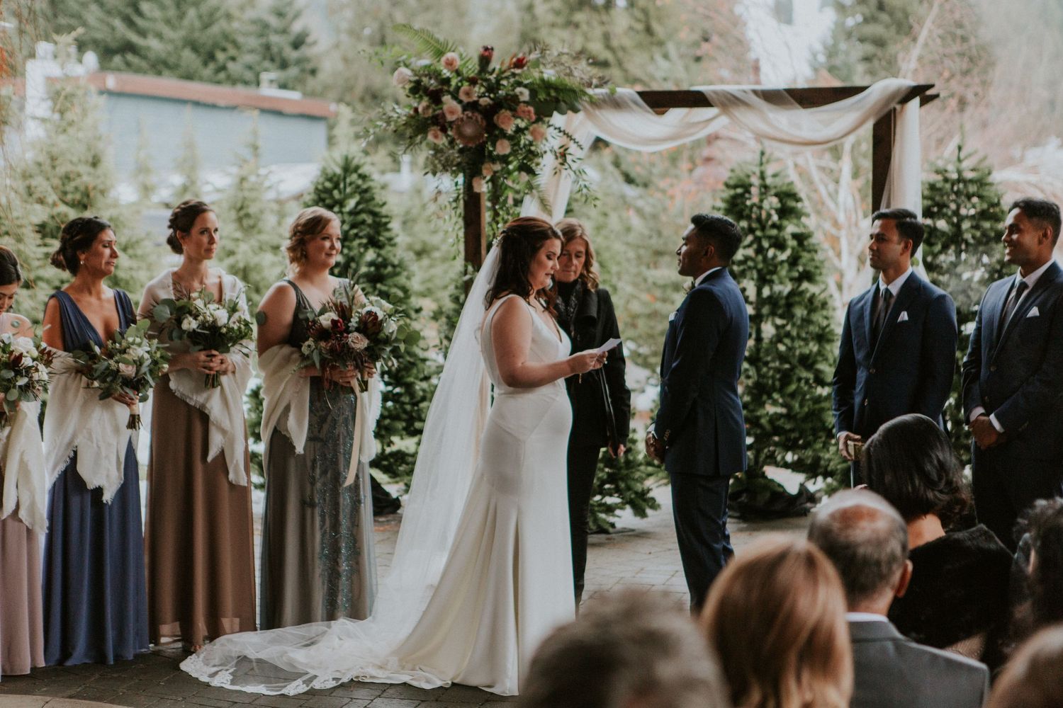 Outdoor garden wedding ceremony with floral arch and wedding party in elegant attire.