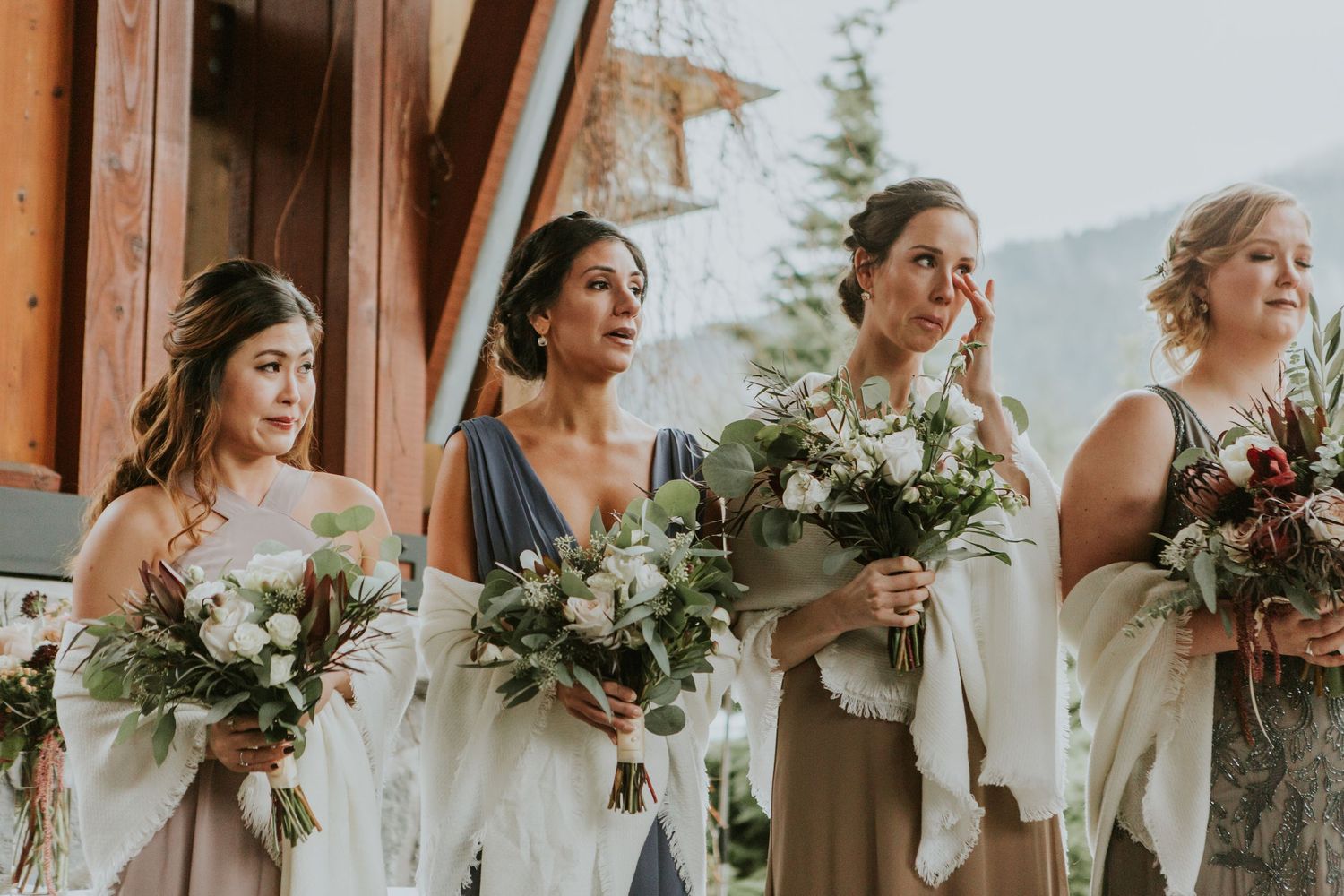A group of bridesmaids in pastel dresses stand together holding lush bouquets of white and green flowers.