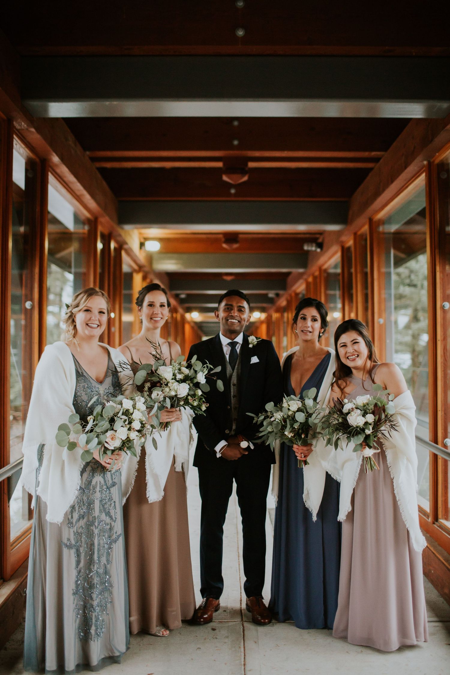 Wedding party poses together in covered walkway holding elegant white floral bouquets.