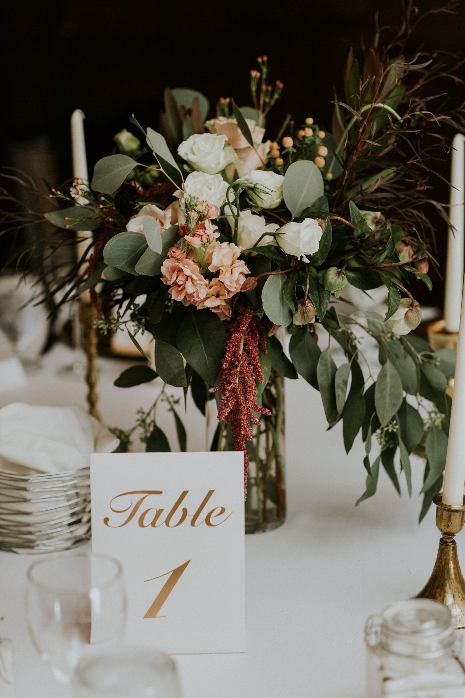 Romantic floral centerpiece with white and blush flowers, eucalyptus leaves, and gold table number.