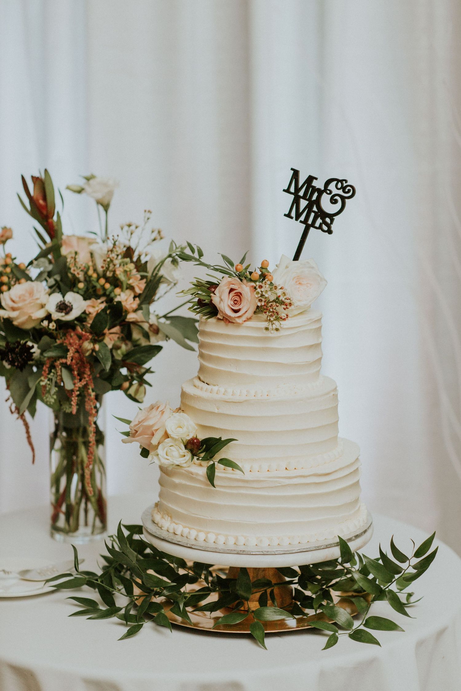 Three-tiered white wedding cake with textured frosting, floral decorations and Mr & Mrs topper.