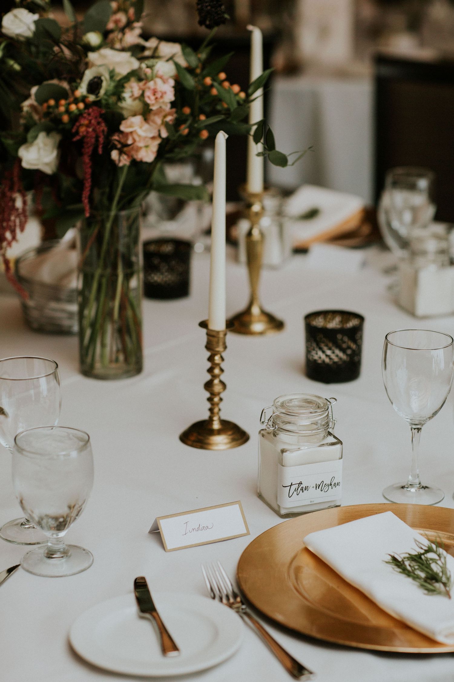 Wedding table setting with brass candlesticks, gold charger plates, and mason jar decorations.