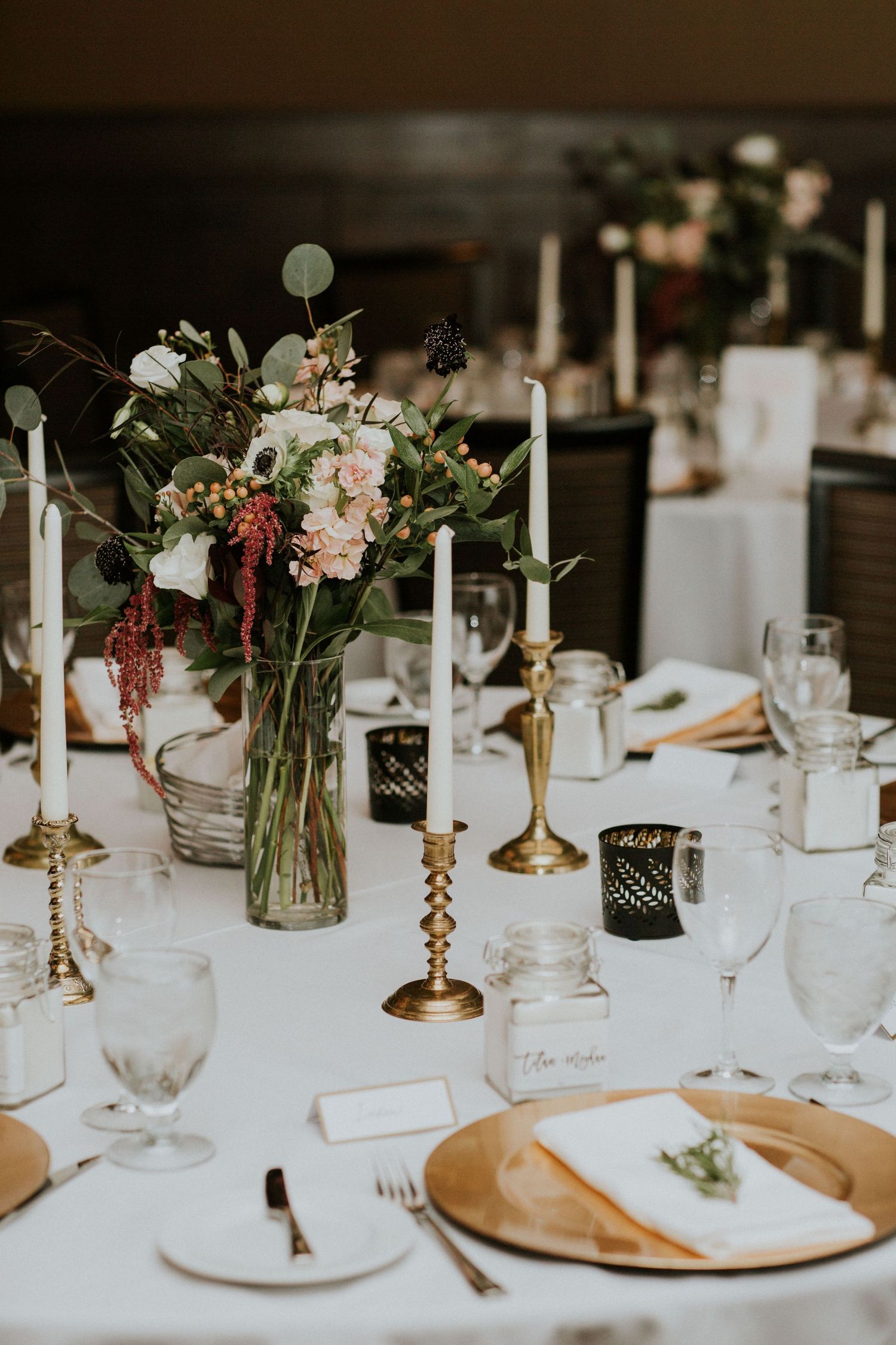 Elegant wedding reception table with floral arrangements, brass candlesticks, and gold accented place settings.