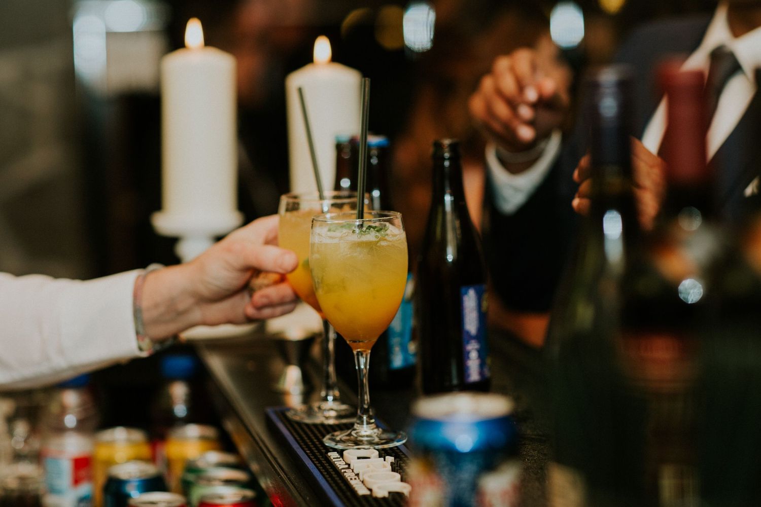Bartender serving a bright orange cocktail in an elegant champagne glass at a dimly lit bar.
