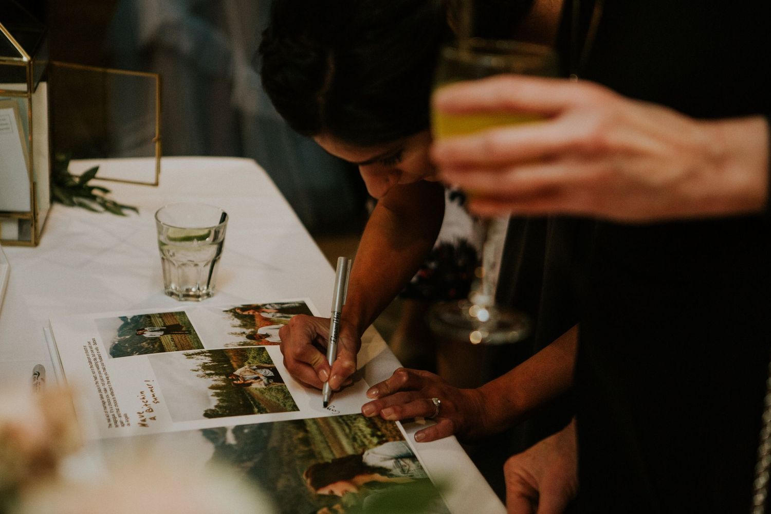 Guest signing a wedding guestbook with photographs at a candlelit reception.
