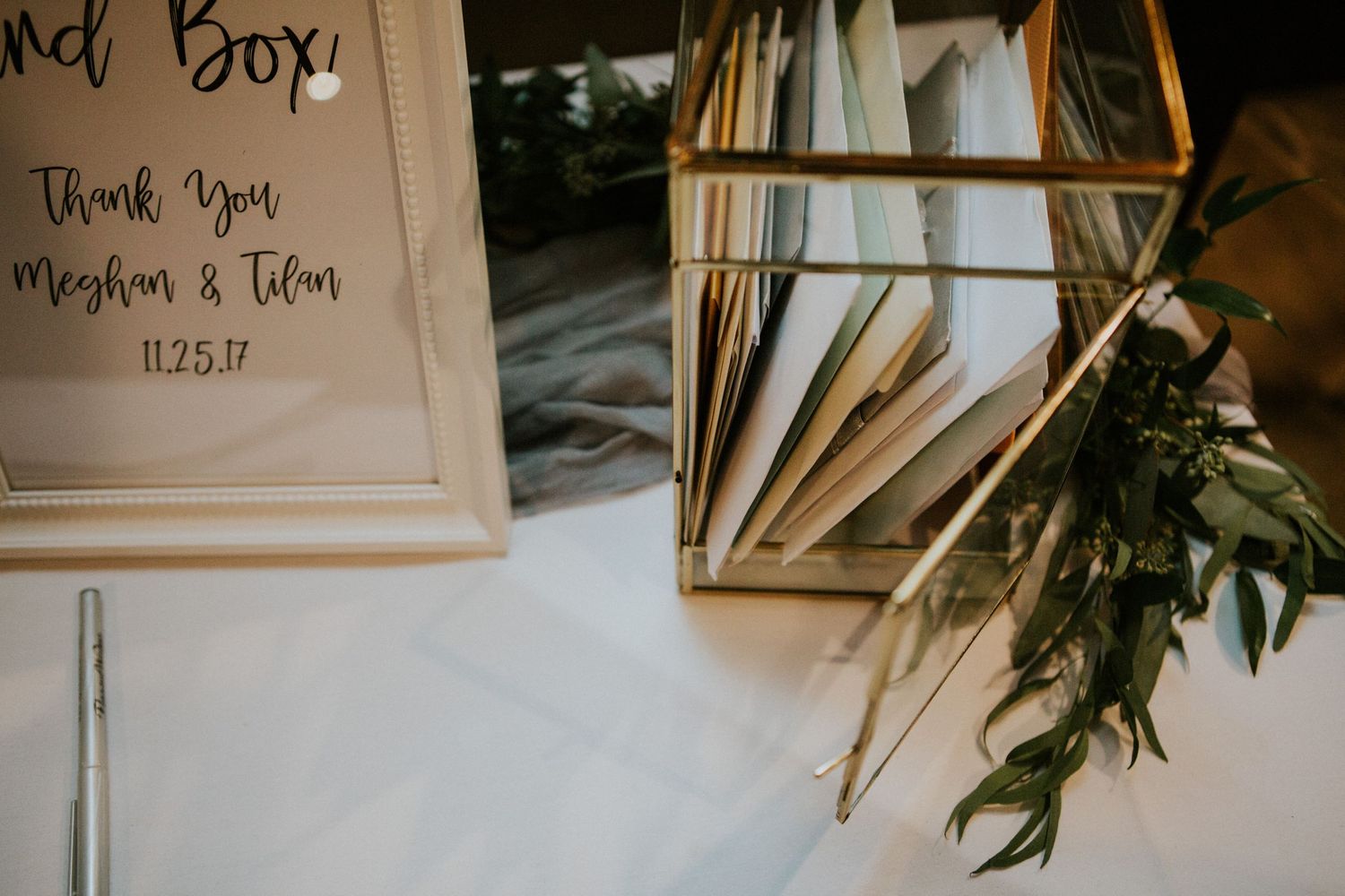 Wedding detail shot of card box and dried palm leaves on white tablecloth.