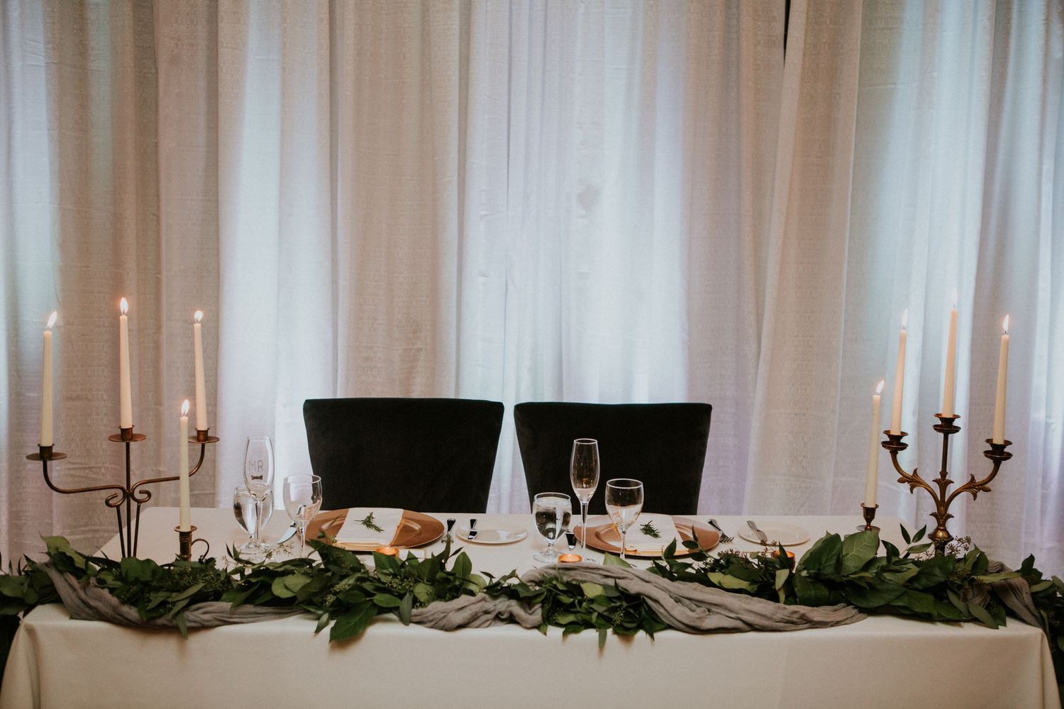 Elegant head table setting with candelabras and greenery garland at wedding reception.