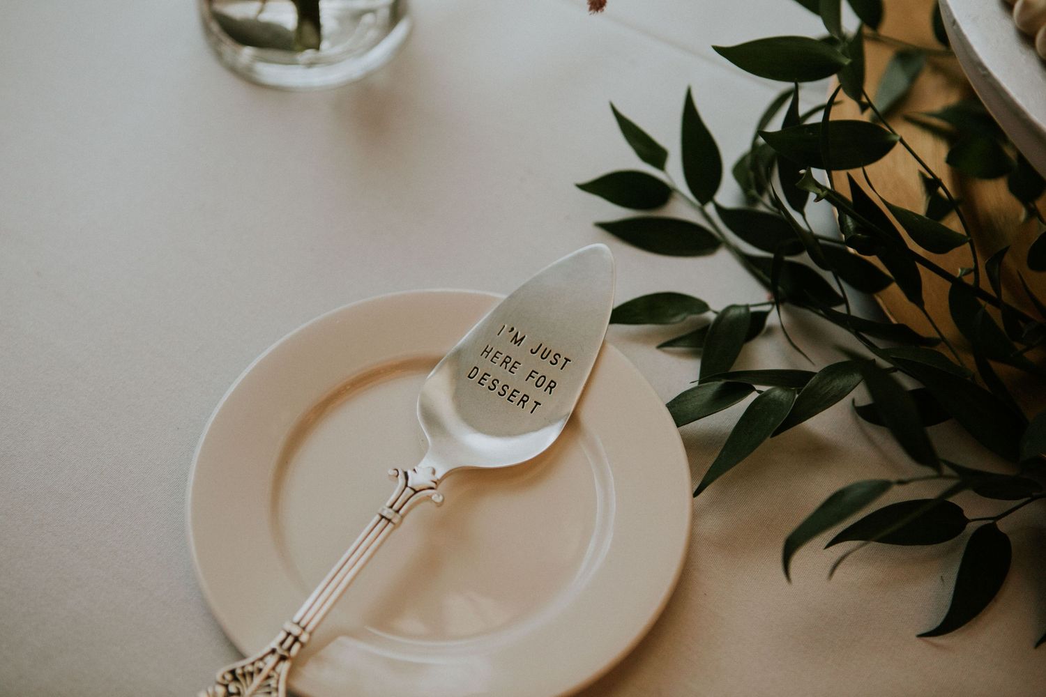 Place setting with engraved silverware and olive branches on white plate.