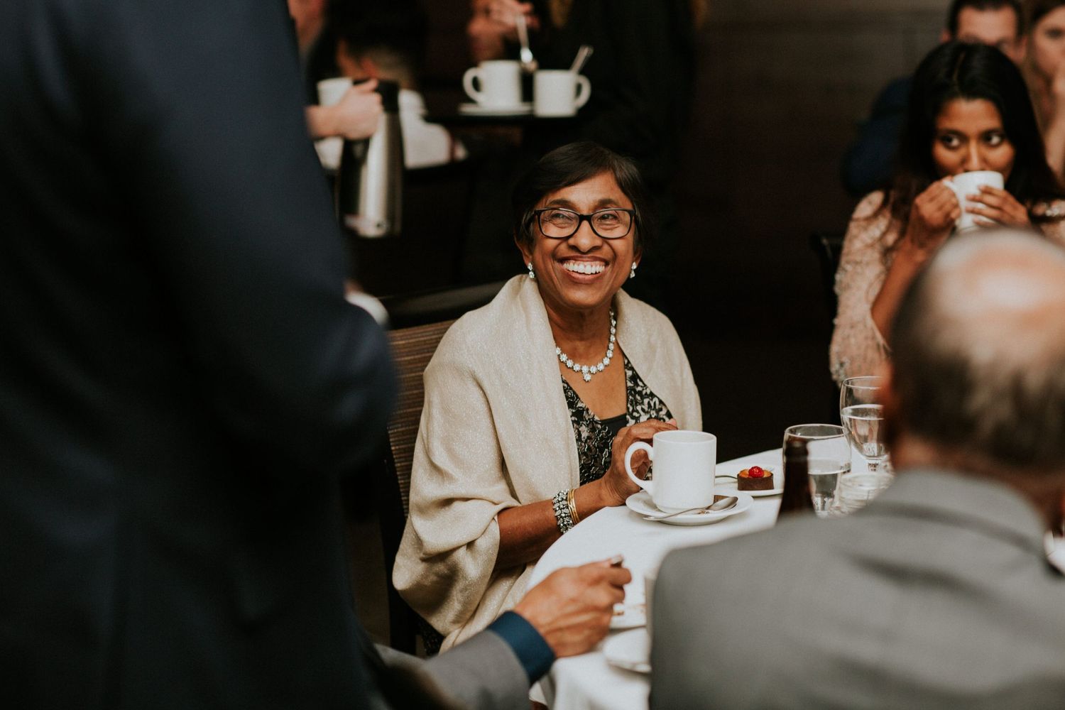 A wedding guest enjoys coffee and conversation at a reception table.