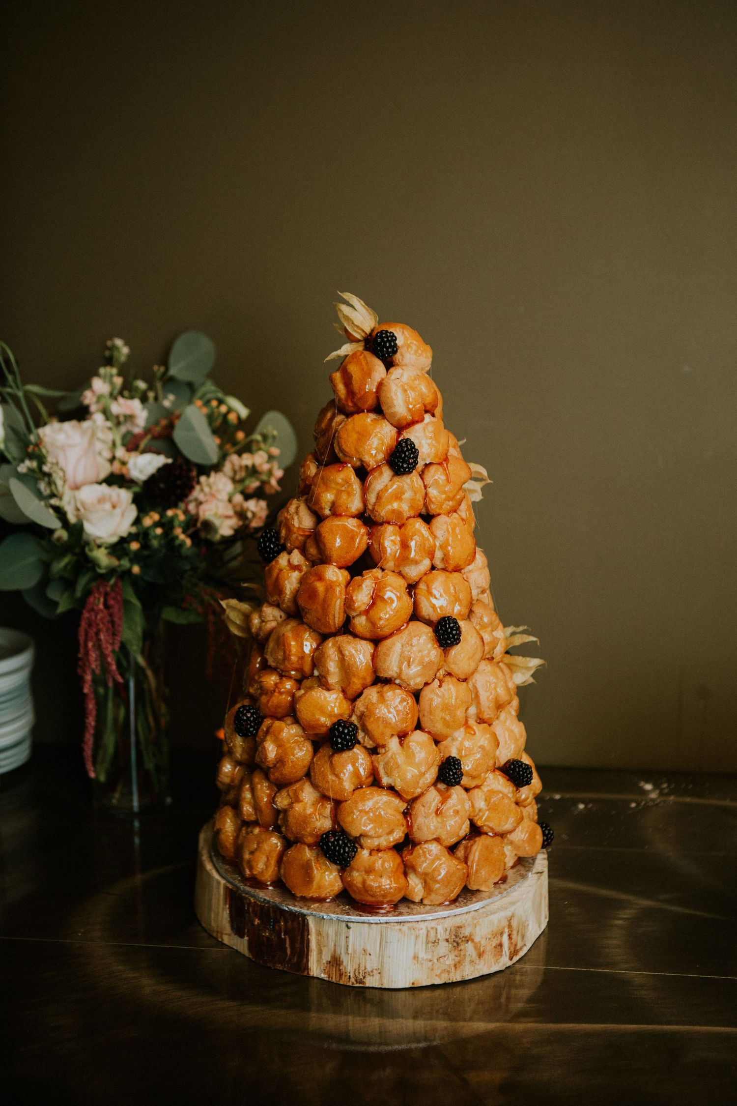 A croquembouche wedding tower decorated with flowers and greenery on a wooden stand.