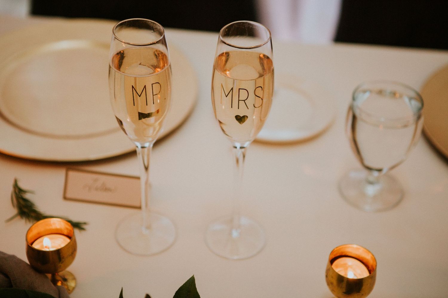 Two champagne flutes labeled Mr and Mrs sit on an elegant table with lit candles.
