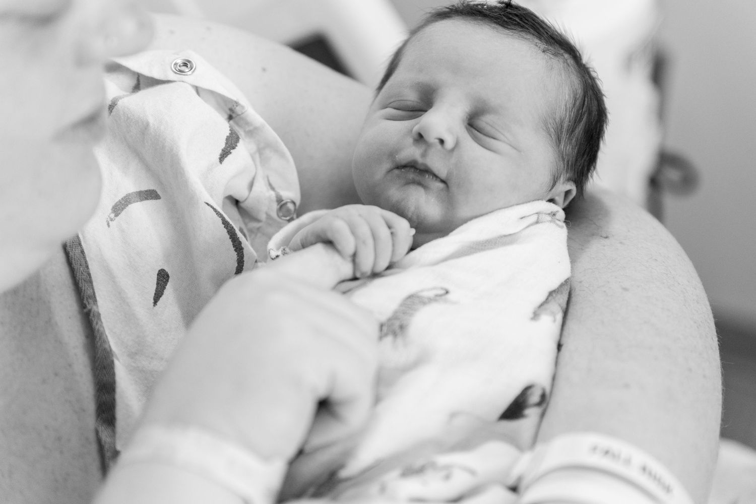 Black and white photo of sleeping newborn baby being cradled in parents arms at hospital.