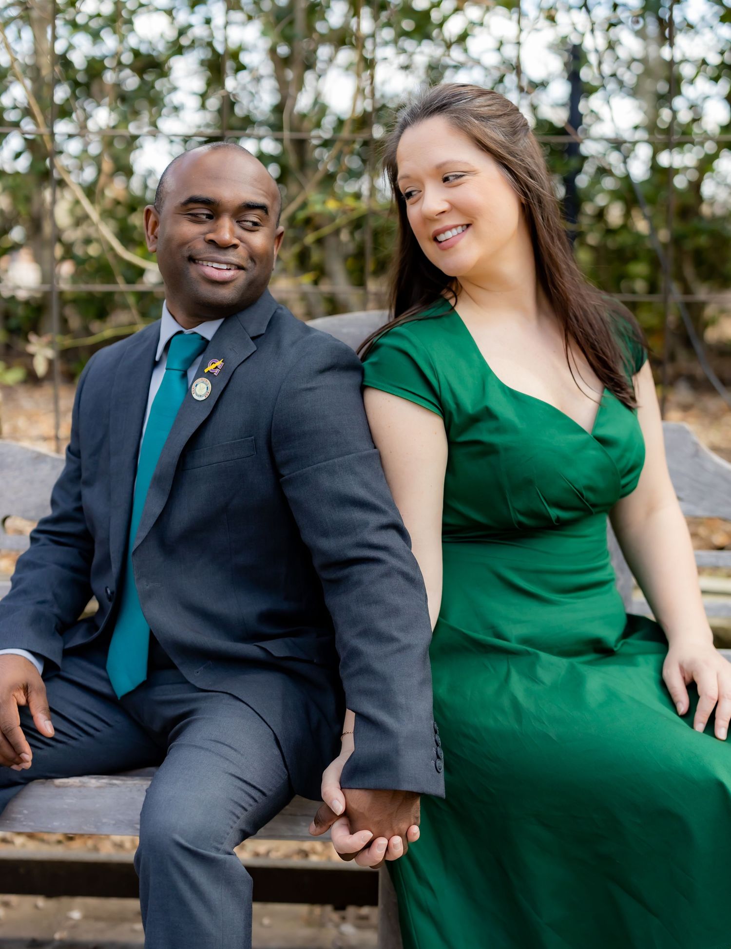 A couple sits together on a wooden bench during an outdoor photo session.