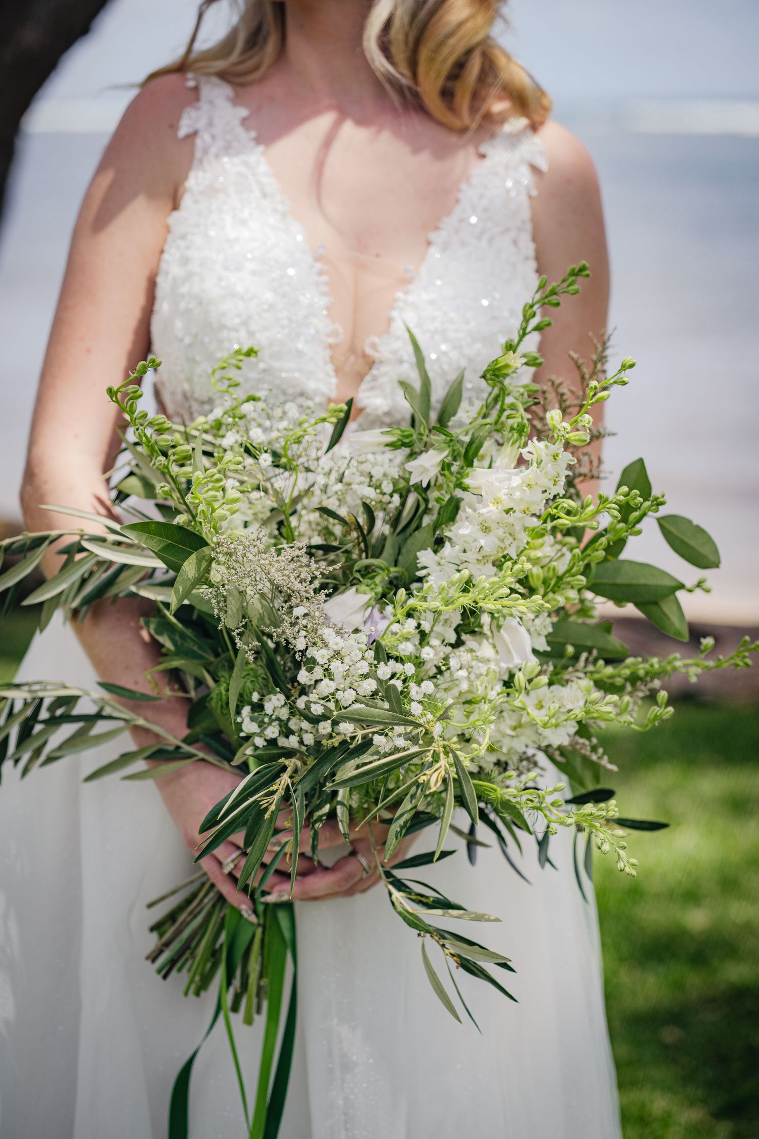 Elegant white bridal bouquet featuring delicate white flowers and cascading greenery against a lace wedding dress.