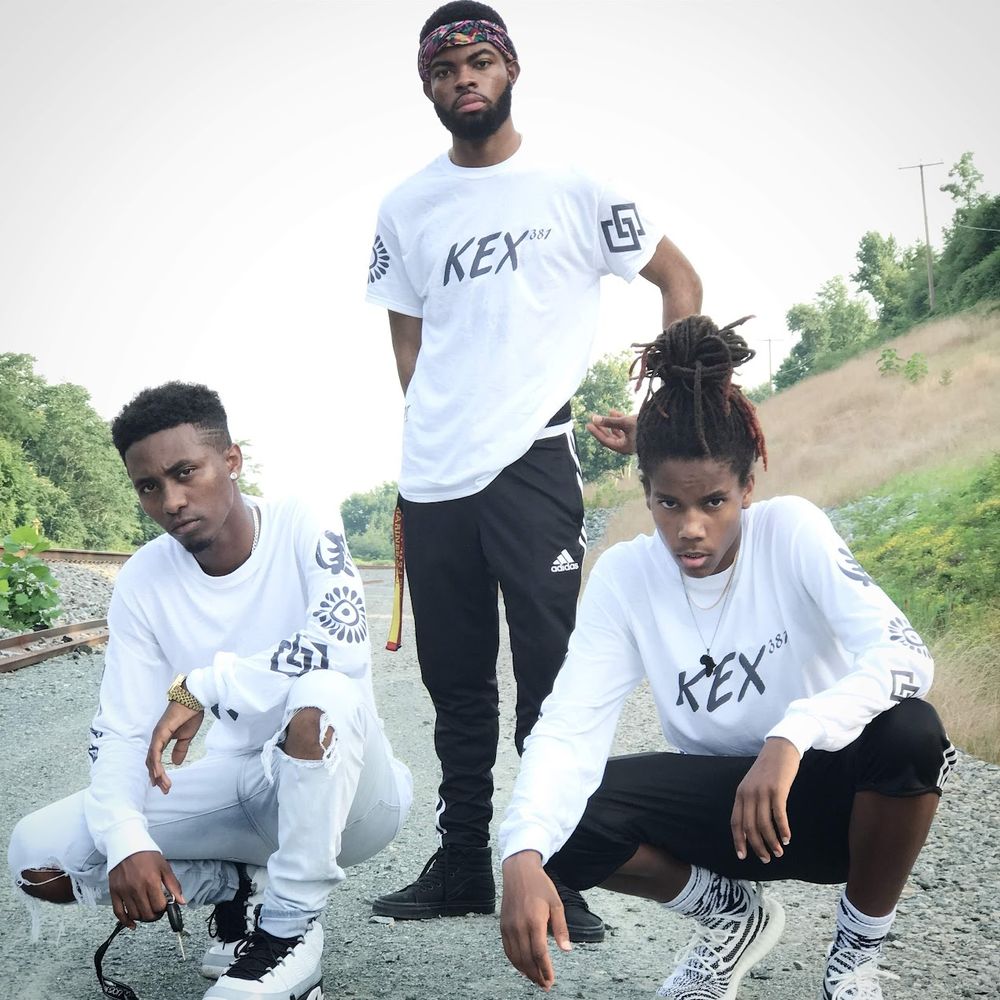 Group wearing matching white REX t-shirts pose together on gravel path.