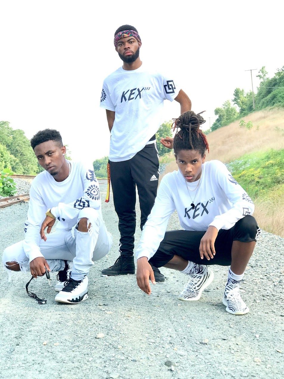 Three people in coordinated white REX outfits pose on gravel path.