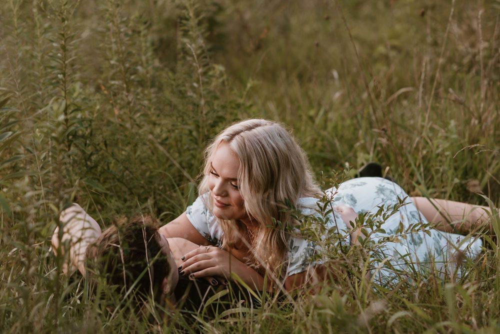 A couple lying together in tall grass during an outdoor photo session.