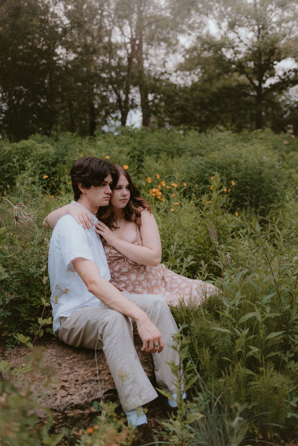 A couple shares an intimate moment while sitting among wildflowers in a garden setting.