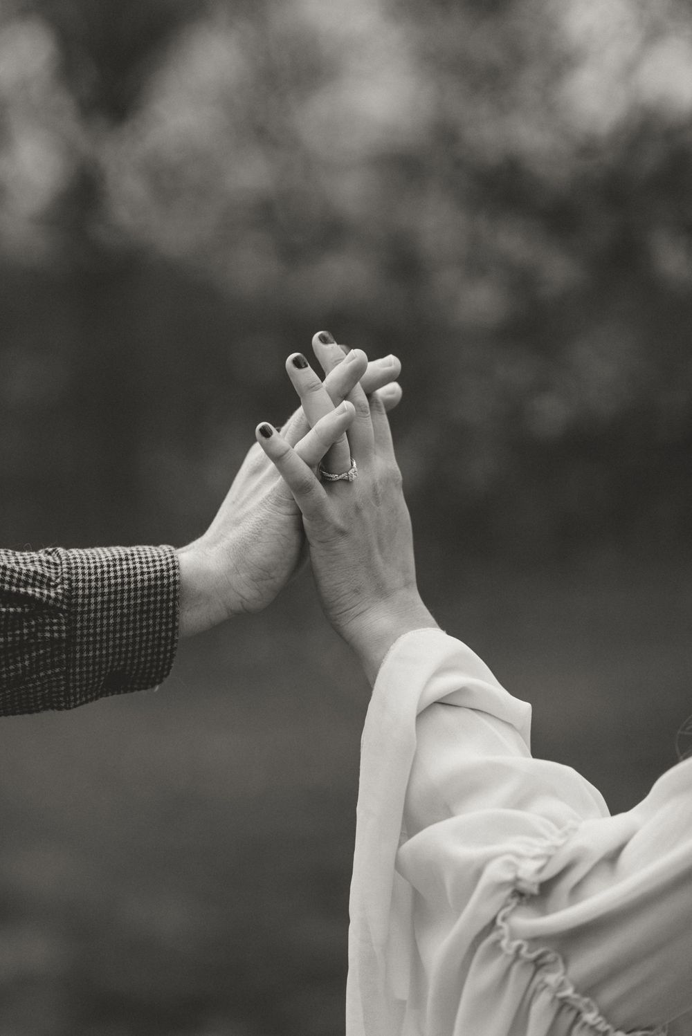 Black and white close-up of hands reaching toward each other against a blurred background.