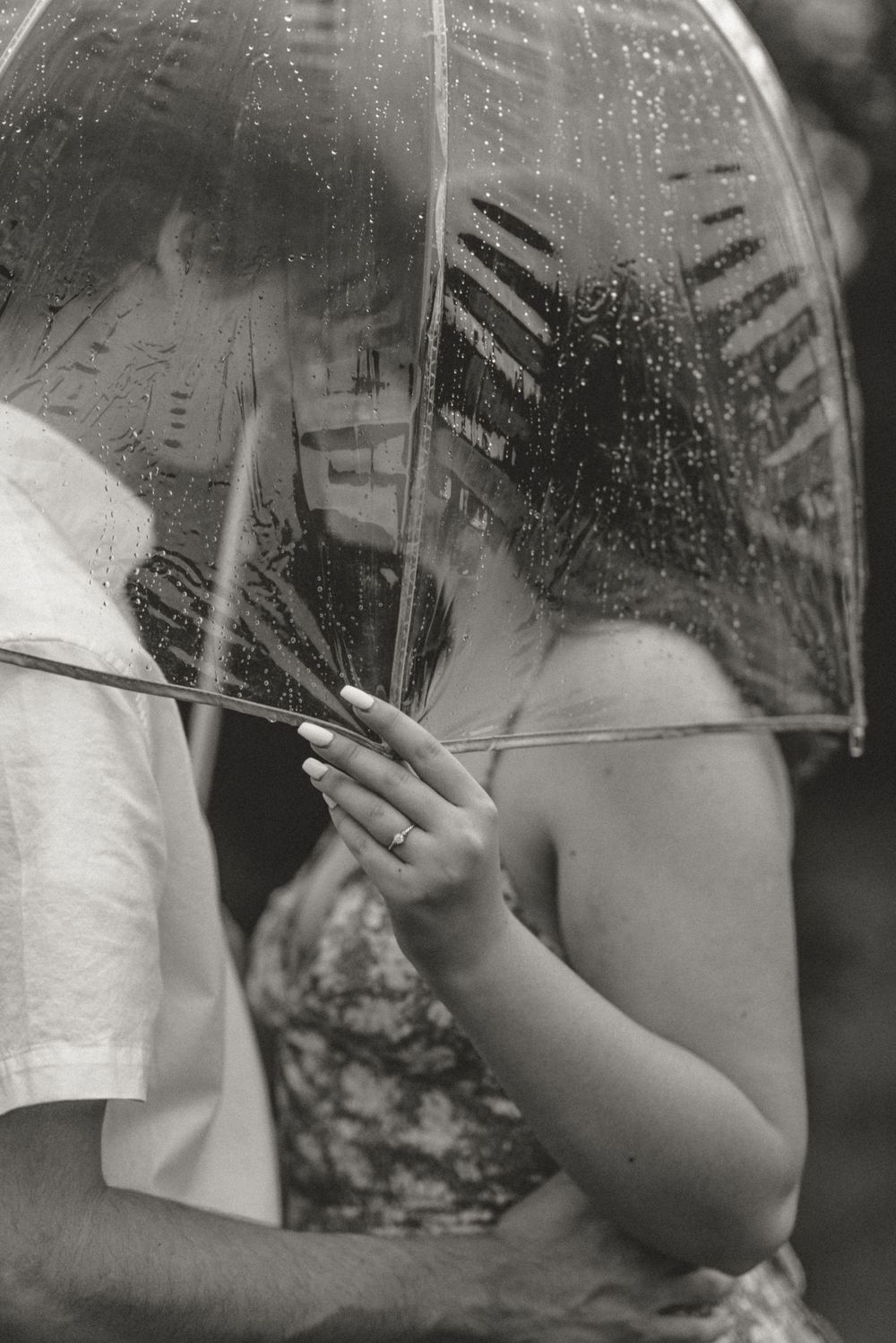 A close-up view through a transparent umbrella showing raindrops and hands.