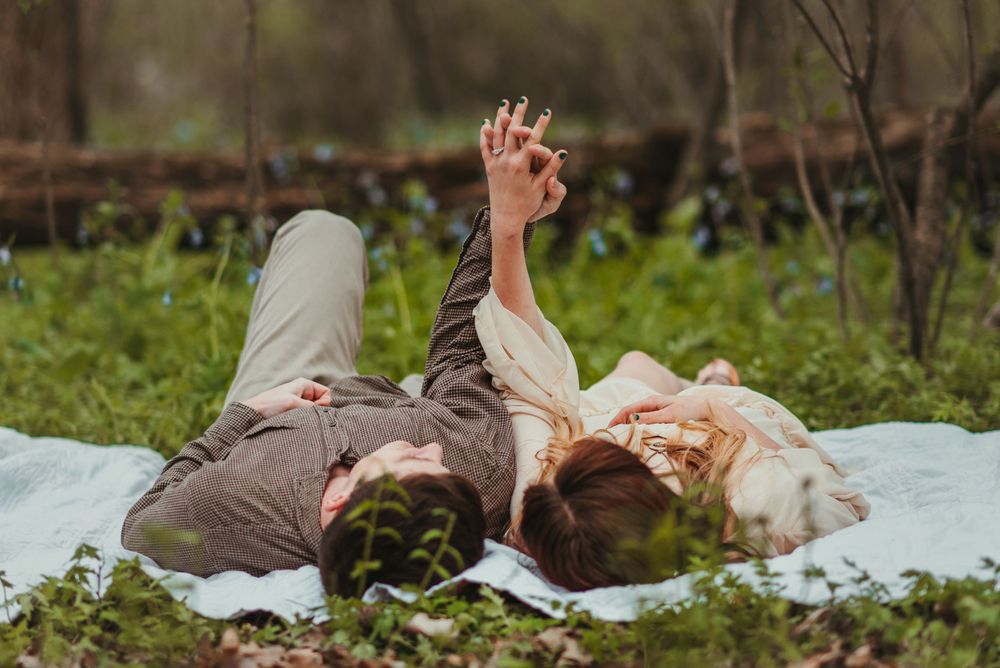 Two people lie on a blanket in a grassy meadow during a spring day.