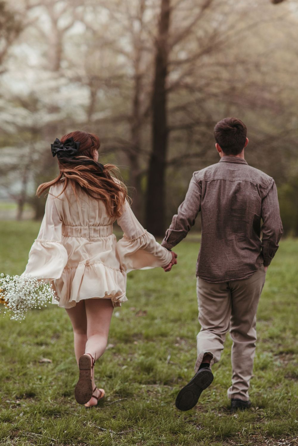 A couple walking through a grassy field holding hands, with soft romantic lighting.