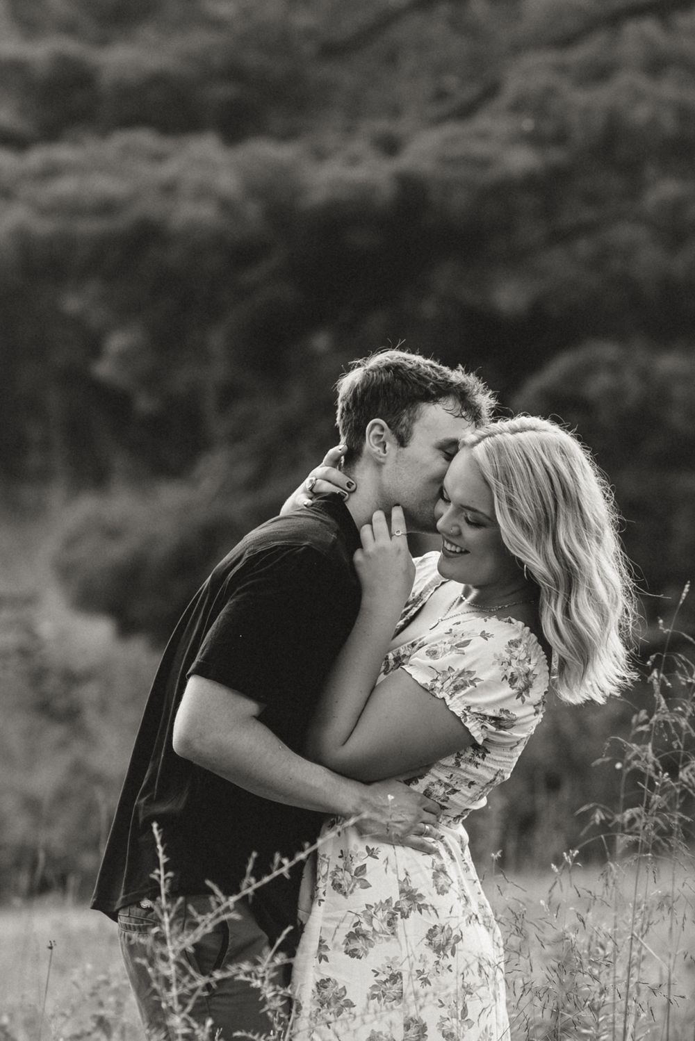 A black and white portrait of a couple sharing an intimate moment in a meadow.