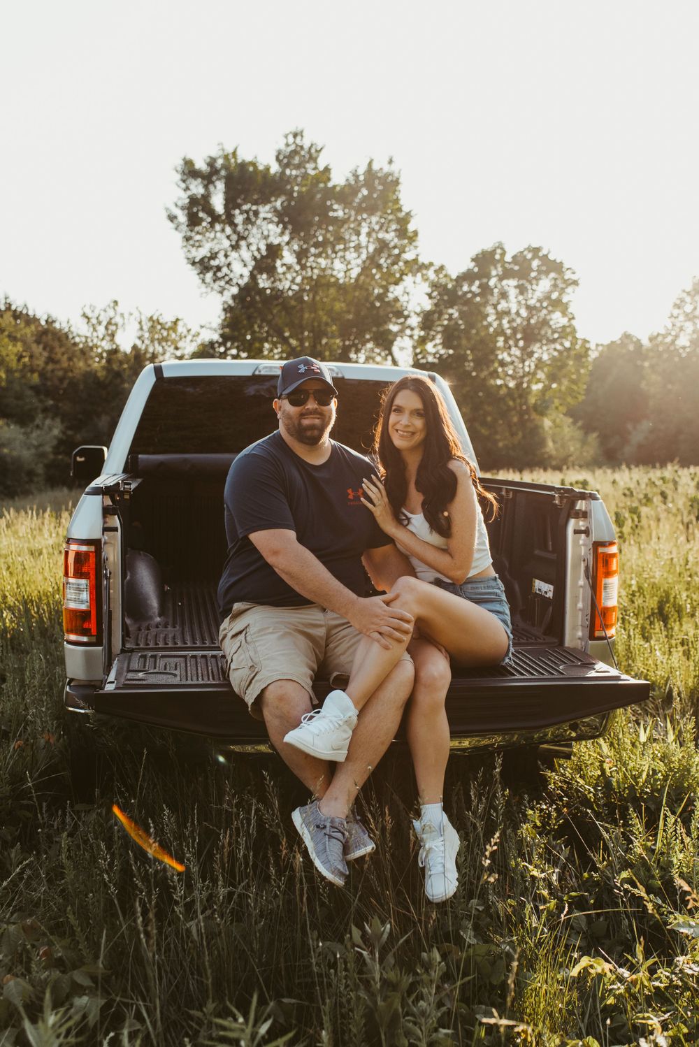 Couple sitting on pickup truck tailgate at sunset in a field of tall grass.