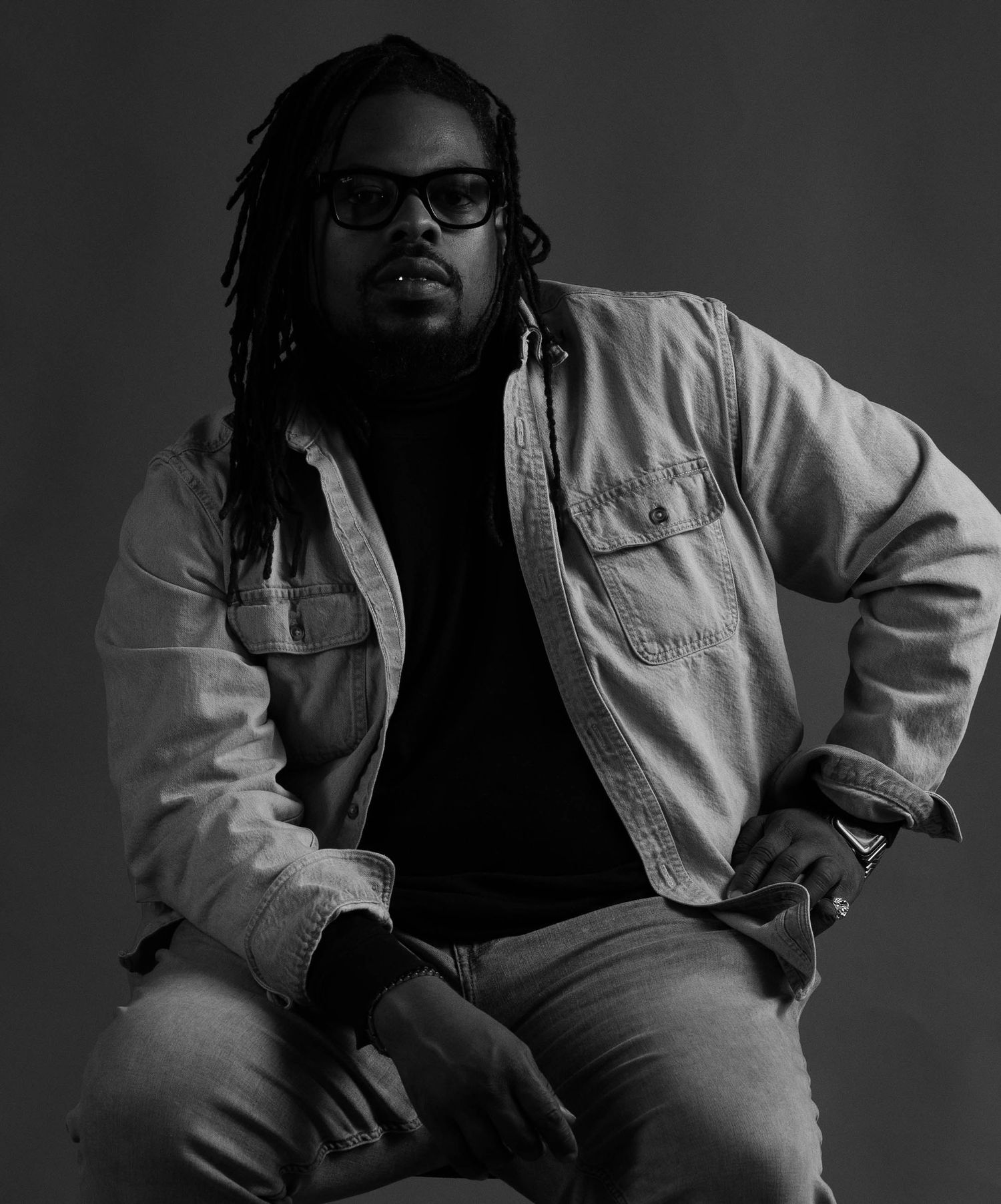 Dramatic black and white portrait of a person in denim jacket and glasses.