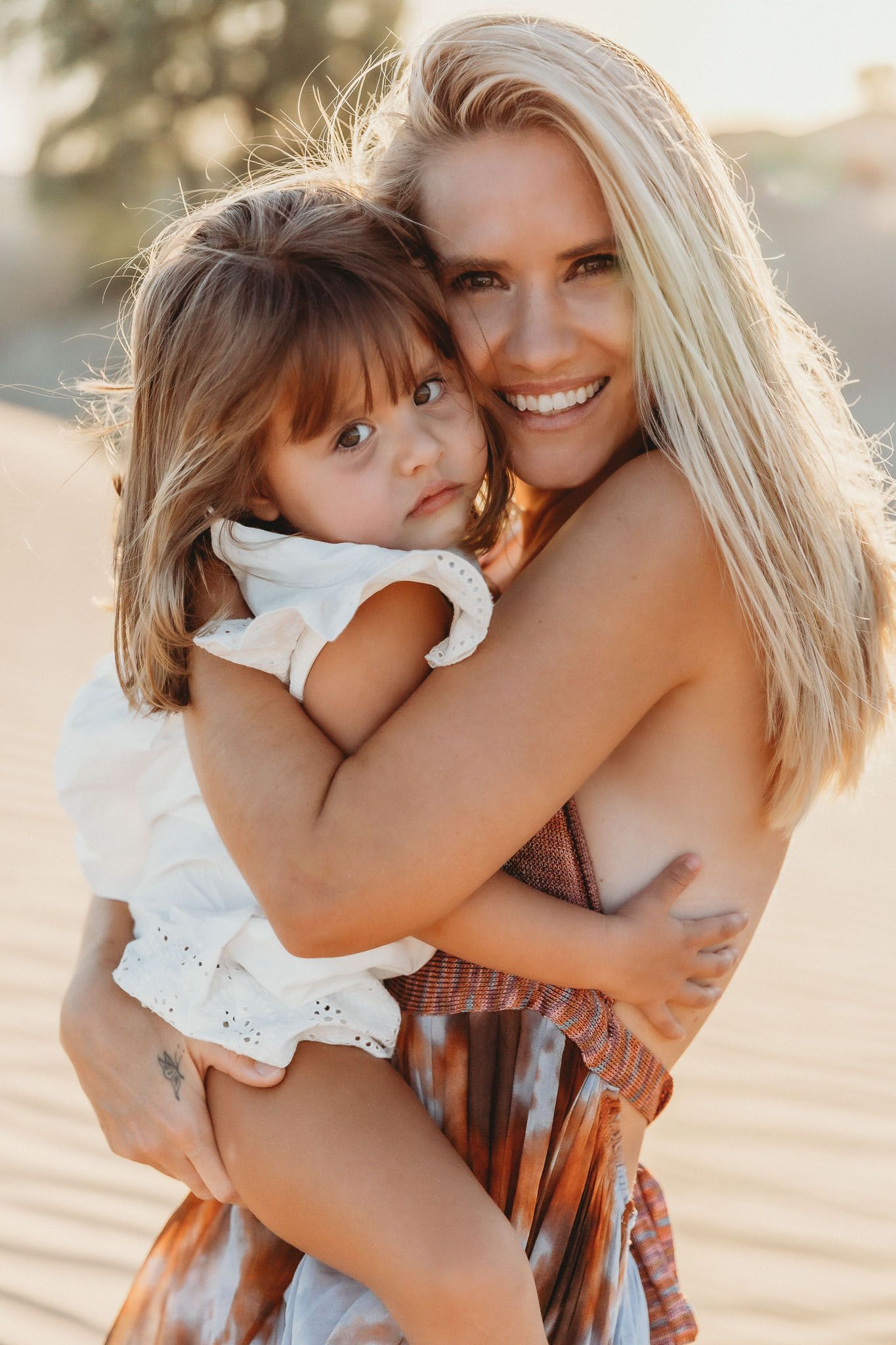 Mother and toddler daughter hugging in Dubai desert at sunset.
