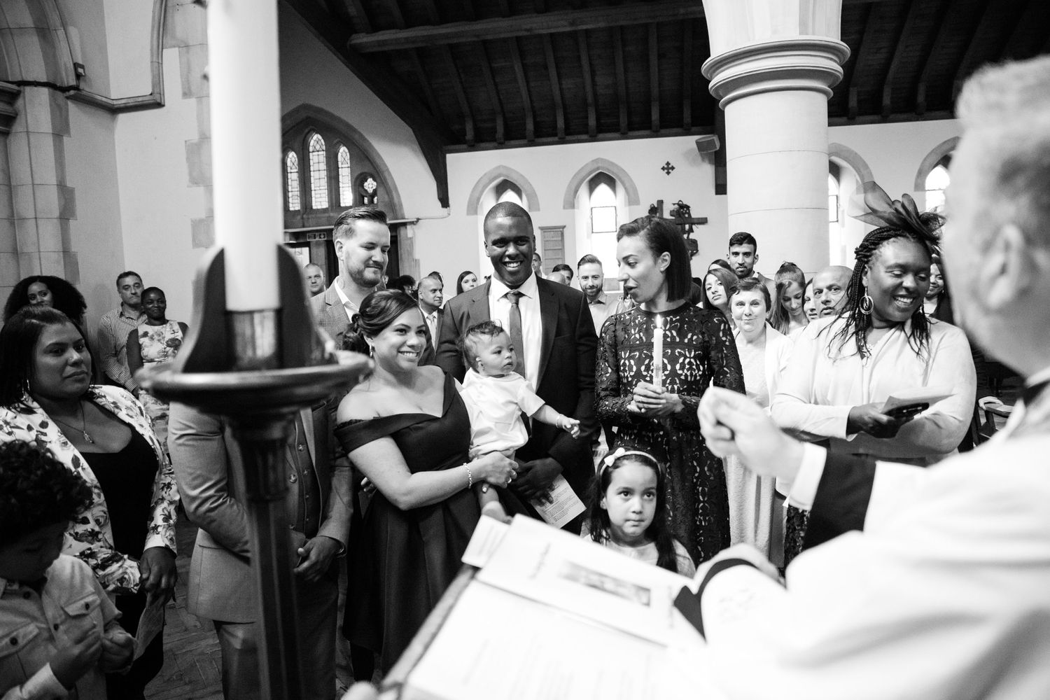 A black and white photo of a baptism ceremony in a church with attendees looking on.