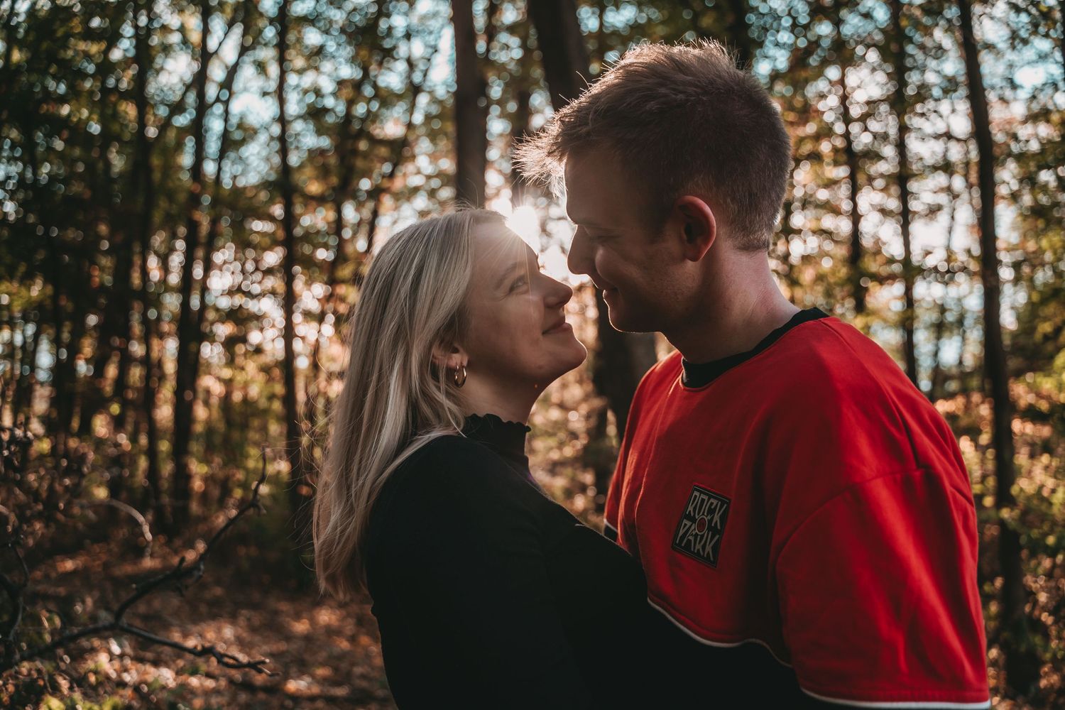 Couple in autumn forest setting with golden sunlight filtering through trees.