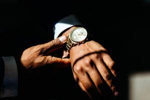 Close-up shot of hands wearing a luxury watch with silver bracelet and white dial against dark background. Middle TN wedding photographer