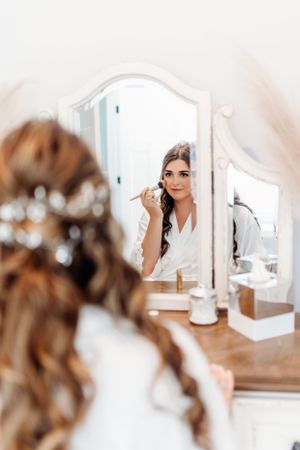 Woman applying makeup while looking in an elegant vanity mirror during wedding preparations. Middle TN wedding photographer