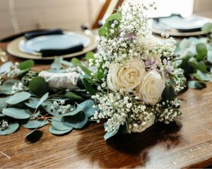 Wedding table decor featuring delicate white flowers and eucalyptus leaves on wooden surface. Middle TN wedding photographer