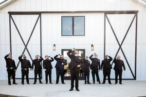 Groomsmen strike playful poses in front of a white barn wedding venue. Middle TN wedding photographer