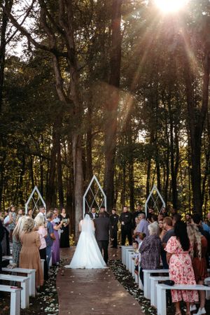 Outdoor forest wedding ceremony with white pillars and guests gathered at sunset. Middle TN wedding photographer