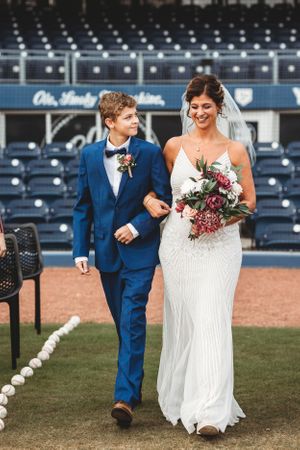Wedding party walking across baseball field with stadium seats in background. Middle TN wedding photographer