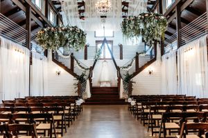 Elegant indoor wedding venue with rustic wooden chairs, white walls, and hanging greenery decorations.Middle TN wedding photographer