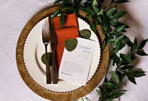 Elegant place settings with gold chargers, greenery, and wedding stationery on white linens. Middle TN wedding photographer