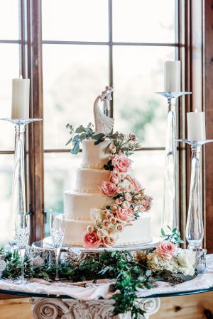 Elegant white wedding cake with pink roses and greenery displayed on a table by large windows. Middle TN wedding photographer