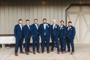 Groomsmen in navy suits and brown shoes sitting on white barn wall for formal wedding photos. Middle TN wedding photographer