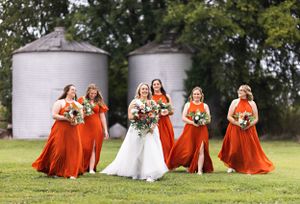 Bridesmaids in vibrant orange dresses pose with the bride on a grassy lawn. Middle TN wedding photographer